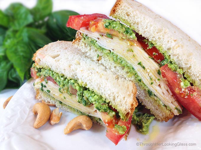a side view of a turkey sandwich made with tomatoes and cashew basil pesto 