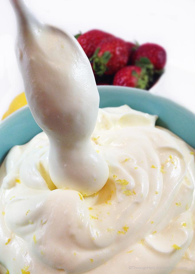 Lemon cream with lemon curd and strawberries in a small blue bowl garnished with lemon zest