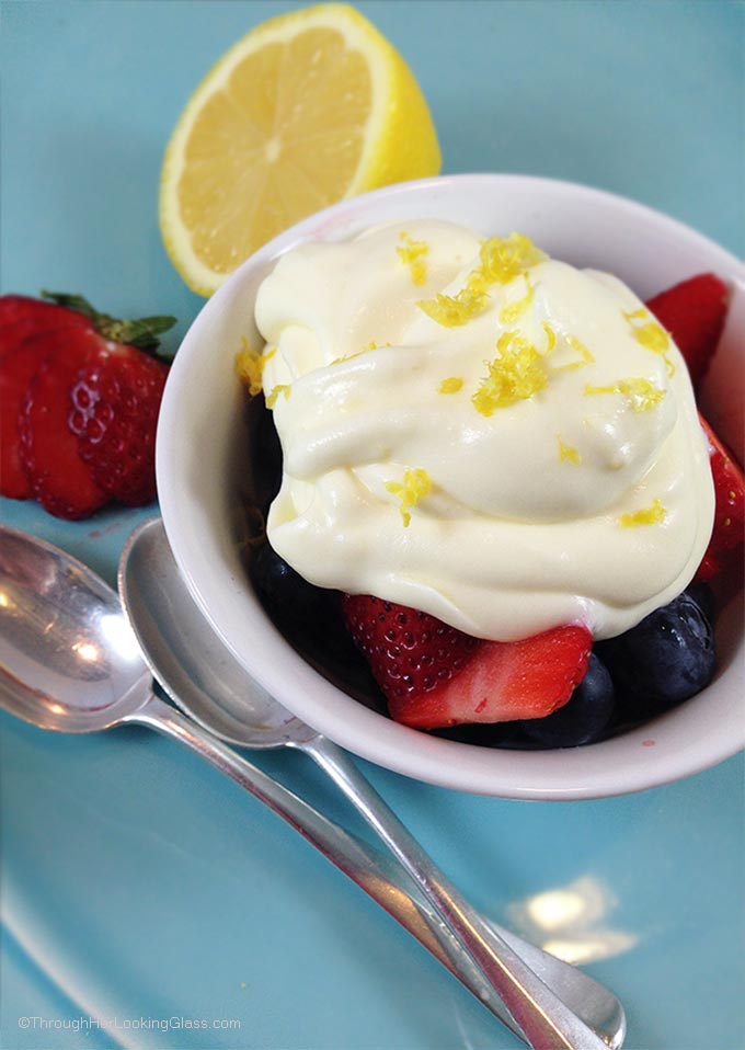 Lemon cream with lemon curd and strawberries in a small blue bowl garnished with lemon zest