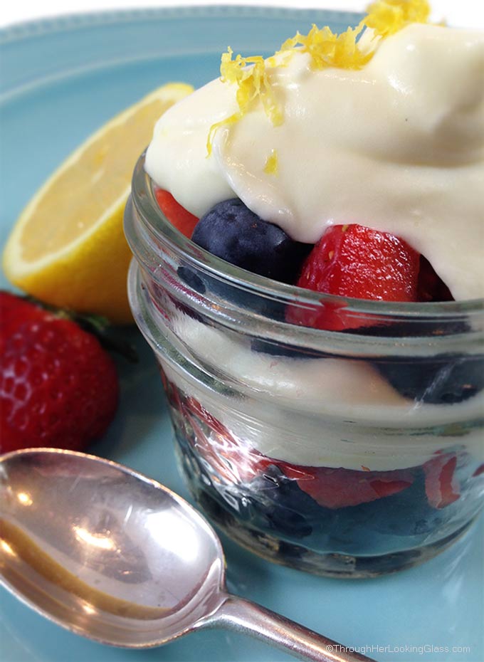 Lemon cream with lemon curd, strawberries, and blueberries in a small glass mason jar garnished with lemon zest